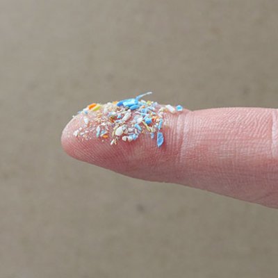 Tiny plastic particles of a range of colours sit atop a fingertip